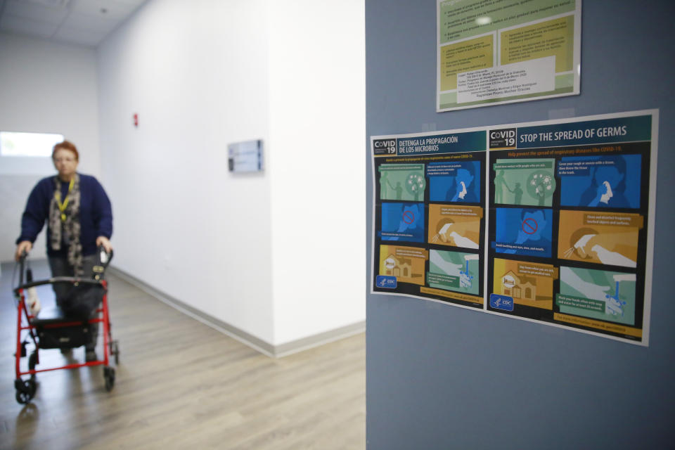 In this March 4, 2020, photo, a senior walks near a sign posted on the wall in Spanish and English informing seniors of the COVID-19 virus and how to "stop the spread of germs" at Little Havana Activities and Nutrition Centers of Dade County, Inc., in Miami. (AP Photo/Brynn Anderson)