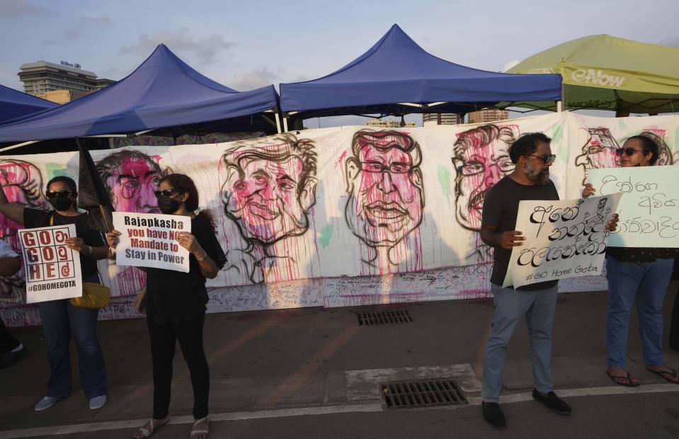 Sri Lankans protest as disfigured portraits of Rajapaksa family members are seen in a banner behind during an ongoing protest in Colombo, Sri Lanka, Wednesday, April 20, 2022. Thousands of Sri Lankans have protested outside President Gotabaya Rajapaksa’s office in recent weeks, demanding that he and his brother, Mahinda, who is prime minister, quit for leading the island into its worst economic crisis since independence from Britain in 1948. (AP Photo/Eranga Jayawardena)