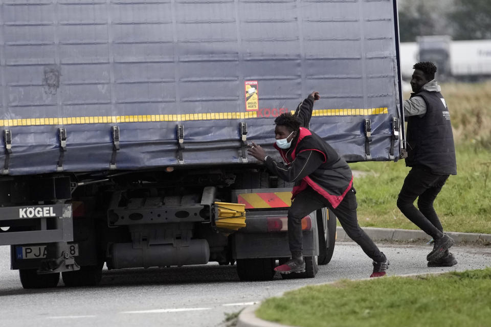 Migrants try to jump on a truck in Calais, northern France, Thursday, Oct. 14, 2021, to cross the tunnel heading to Britain. In a dangerous and potentially deadly practice, they are trying to get through the heavily policed tunnel linking the two countries by hiding on a truck. (AP Photo/Christophe Ena)