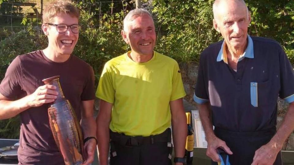 The smiling winner of the Welsh race Matthew Atkinson holding the trophy beside experienced runner Colin Donnelly and Joss. It is a sunny day and there are trees in the background