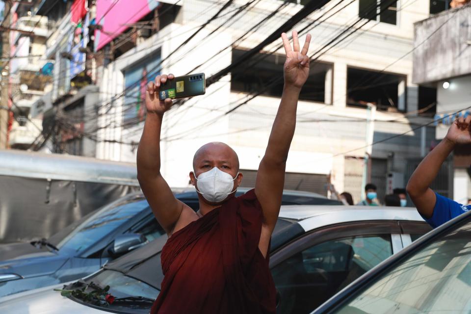 A Buddhist monk flashes the three-fingered salute as he watches protesters march in Yangon, Myanmar on Sunday, Feb. 7, 2021. Thousands of people rallied against the military takeover in Myanmar's biggest city on Sunday and demanded the release of Aung San Suu Kyi, whose elected government was toppled by the army that also imposed an internet blackout. (AP Photo)