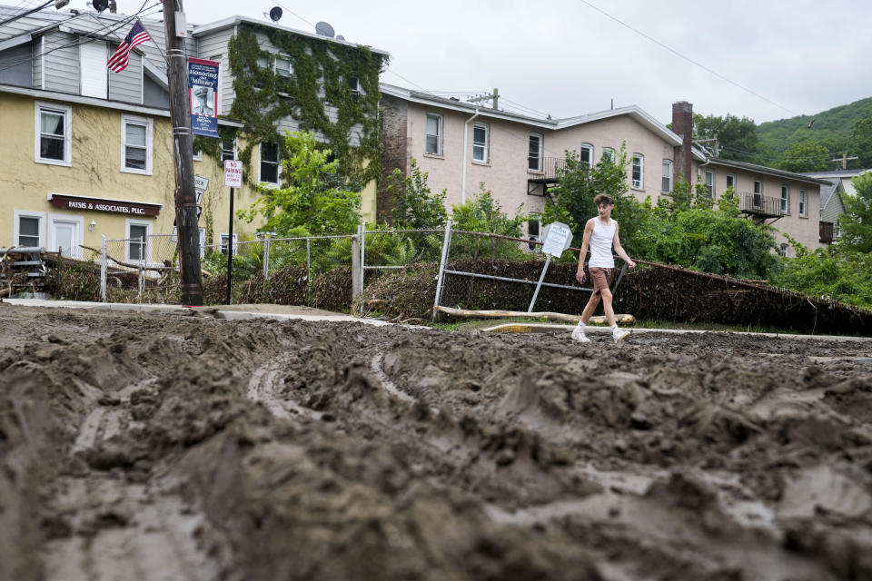 Pedestrians pass along Main Street damaged by flooding the previous day, Monday, July 10, 2023, in Highland Falls, N.Y. Heavy rain has washed out roads and forced evacuations in the Northeast as more downpours were forecast throughout the day. One person in New York's Hudson Valley has drowned as she was trying to leave her home. (AP Photo/John Minchillo)