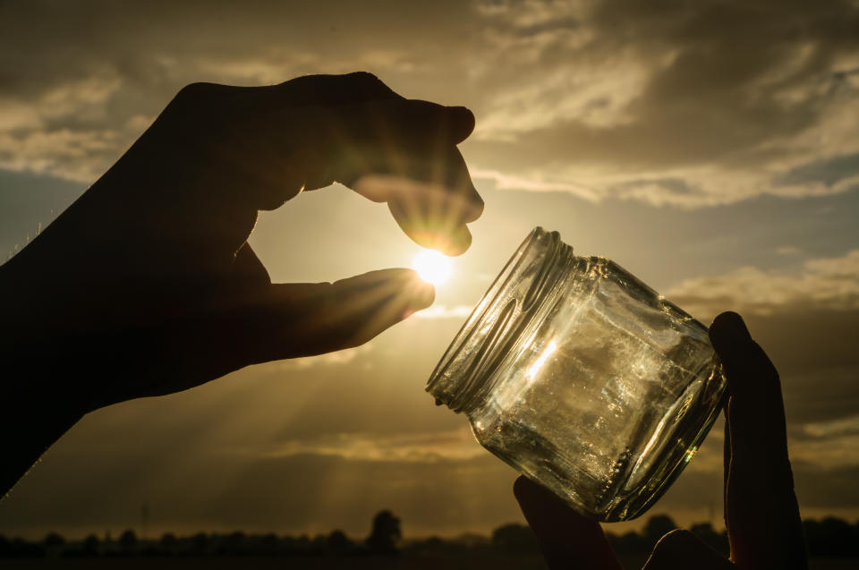 Person holding a jar against a sunny sky.