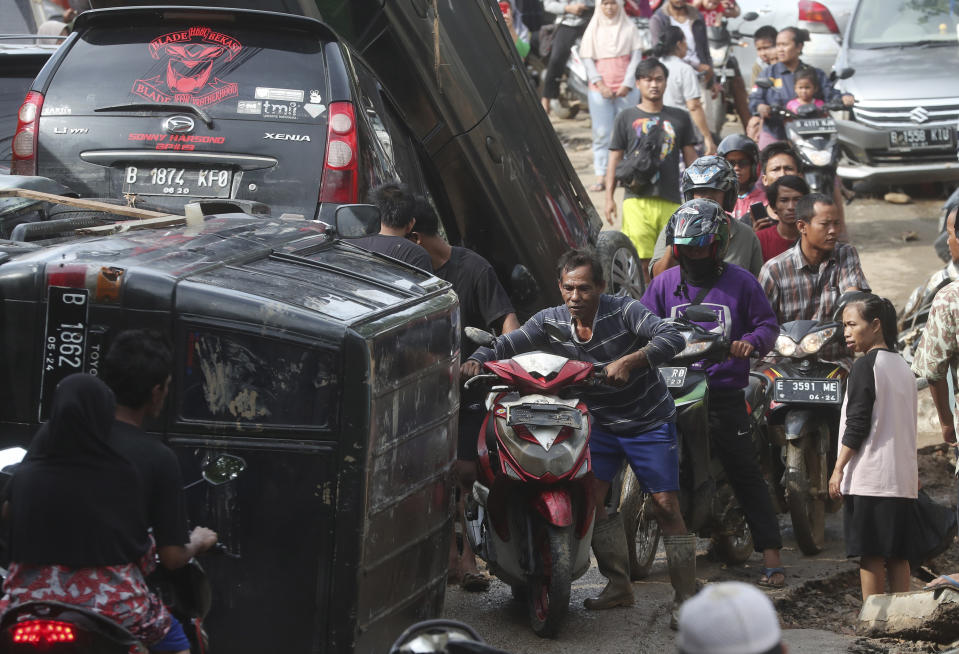 Residents walk near the wreckage of cars that were swept away by flood in Bekasi, West Java, Indonesia, Friday, Jan. 3, 2020. Severe flooding in greater Jakarta has killed scores of people and displaced tens of thousands others, the country's disaster management agency said. (AP Photo/Achmad Ibrahim)