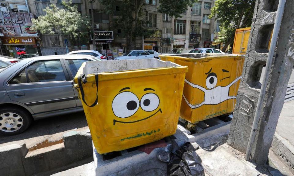 Two large litter bins with cartoon faces painted on them, one of the faces wearing a mask
