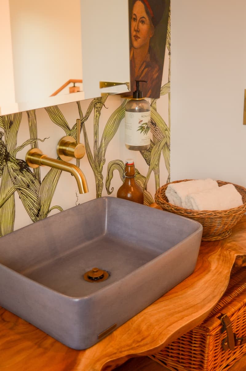 Sink seen in bathroom with live wood shelves and corn wallpaper.