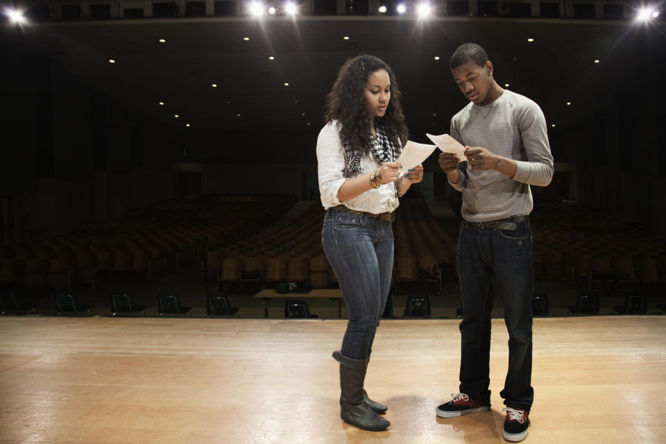 Two people are reading papers on an empty theater stage, possibly rehearsing lines