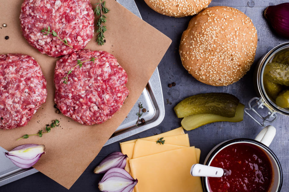 Raw hamburgers with American cheese and other condiments on the side