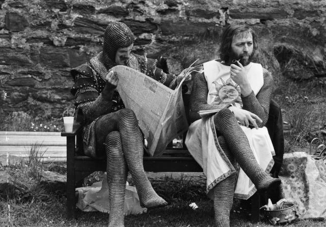 21st May 1974:  A chainmail-clad John Cleese reads a newspaper while Graham Chapman smokes a quiet pipe on the set of &#39;Monty Python and the Holy Grail&#39;.  (Photo by John Downing/Express/Getty Images)