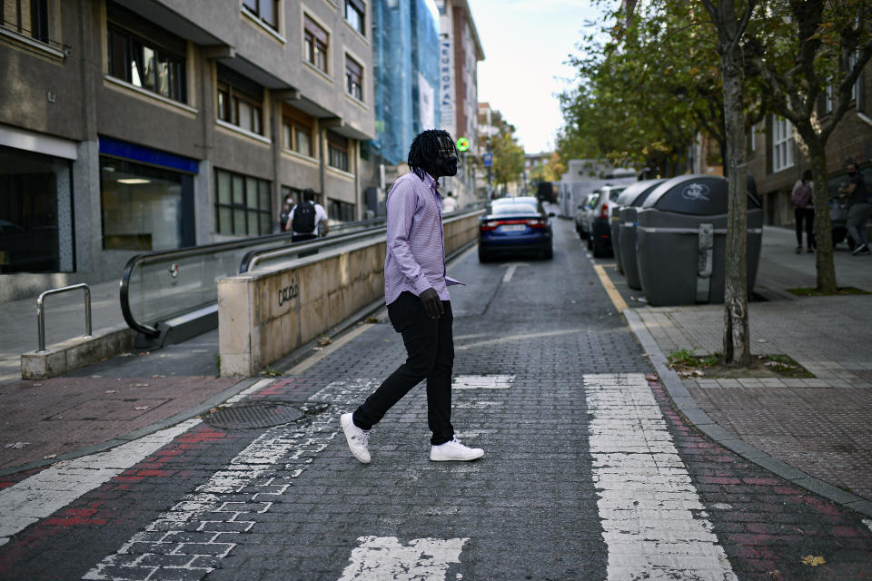 Mbaye Babacar Diouf, wears a face mask to protect against coronavirus, as he crosses a street in the basque city of Algorta, northern Spain, Wednesday, Nov. 18, 2020. Mbaye Babacar Diouf's life as a migrant in Europe took a turn for the better when he was adopted in Spain at the age of 28. That enabled him to pay his debts to human traffickers, study nursing and find a job at a Spanish hospital. Now he's giving back to the community. In a Bilbao hospital he cares for COVID-19 patients. (AP Photo/Alvaro Barrientos)