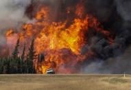 Smoke and flames from the wildfires erupt behind a car on the highway near Fort McMurray, Alberta, Canada, May 7, 2016. REUTERS/Mark Blinch/File Photo