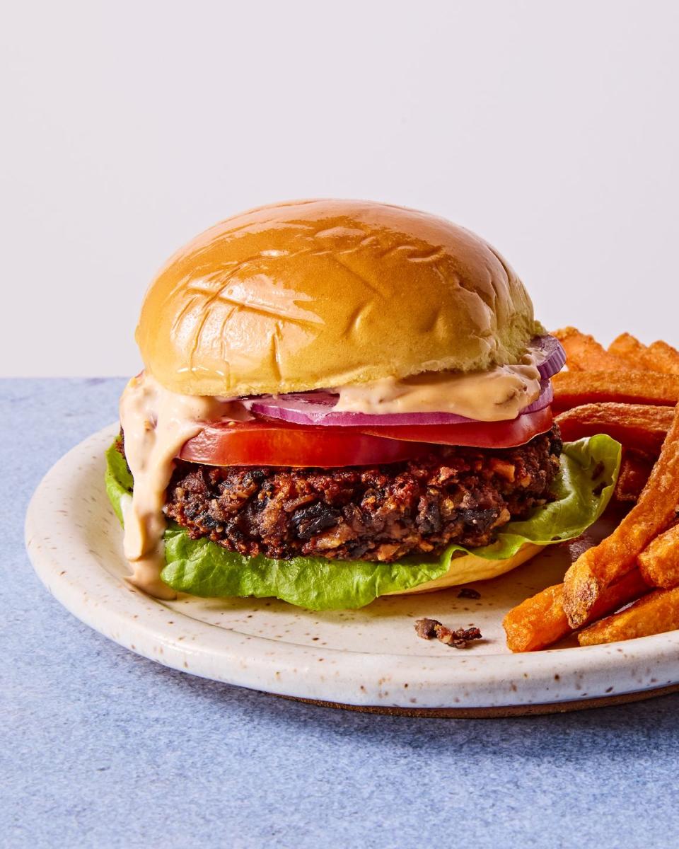 veggie burger topped with lettuce, tomato, red onion, and chipotle mayo on a plate with sweet potato fries