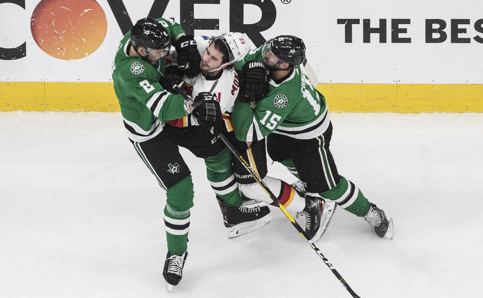 Calgary Flames' Sean Monahan (23) is checked by Dallas Stars' Jamie Oleksiak (2) and Blake Comeau (15) during the third period of a first round NHL Stanley Cup playoff hockey series in Edmonton, Alberta, on Thursday, Aug. 13, 2020. (Jason Franson/The Canadian Press via AP)