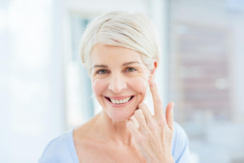 Gray-haired woman that's smiling and applying apple cider vinegar skin care to her face