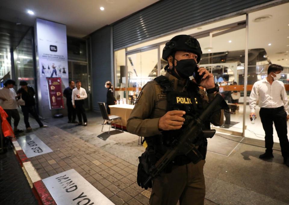 An armed police officer speaks on a mobile phone as he leaves the Siam Paragon shopping mall (EPA)