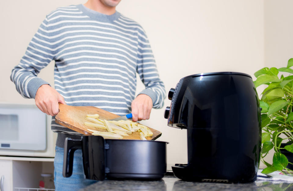 Man at home using air fryer to fry sliced potatoes. (PHOTO: Getty Images)