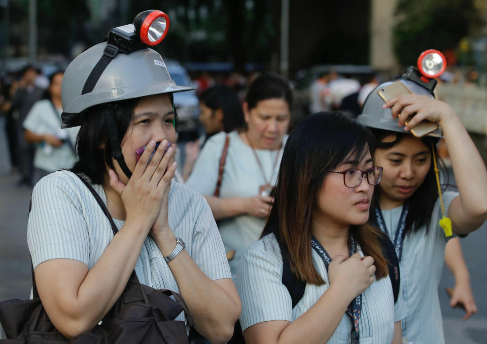 In this April 22, 2019, file photo, wearing protective helmets, employees evacuate their office building following an earthquake in Manila, Philippines. (AP Photo/Aaron Favila, File)