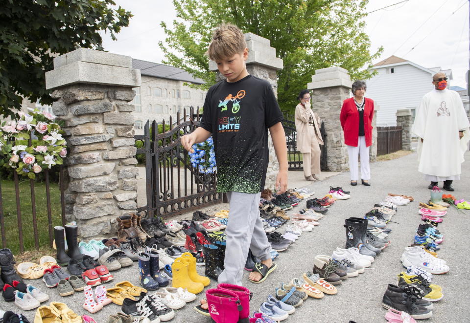 Jamieson Kane puts down tobacco as a tribute to all the victims of the residential school system as he walks amongst children's shoes outside St. Francis Xavier Church in Kahnawake, Quebec, Sunday, May 30, 2021. (Graham Hughes/The Canadian Press via AP)