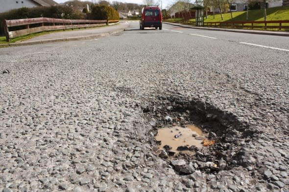 Large deep pothole an example of poor road maintance due to reducing local council repair budgets