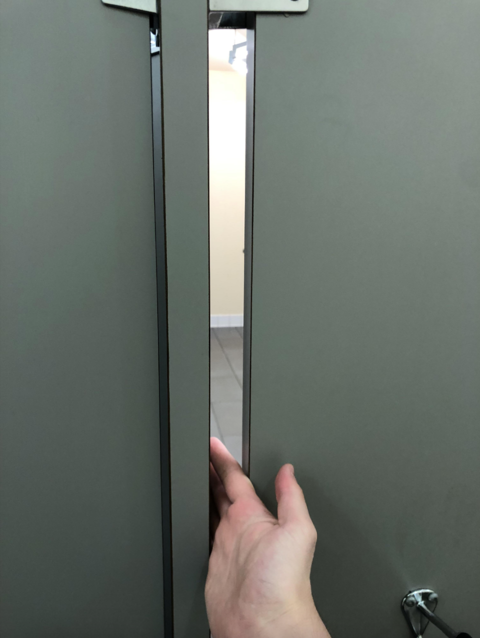 Person's hand pushing a stall door slightly ajar in a restroom, highlighting a privacy concern