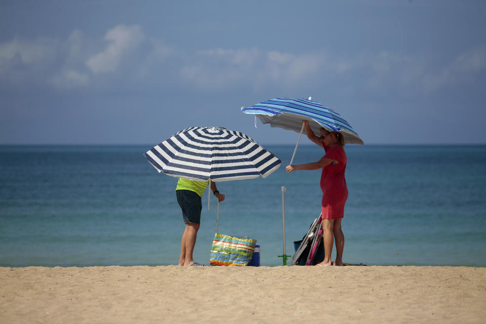 A couple adjust sunshades at the beach of Palma de Mallorca, Spain, Tuesday, June 16, 2020. Borders opened up across Europe on Monday after three months of coronavirus closures that began chaotically in March. But many restrictions persist, it's unclear how keen Europeans will be to travel this summer and the continent is still closed to Americans, Asians and other international tourists. (AP Photo/Joan Mateu)