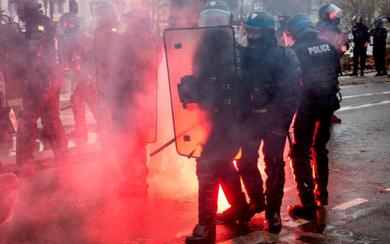 Riot police members walk forward carrefully past a flare lying on the ground during a protest of