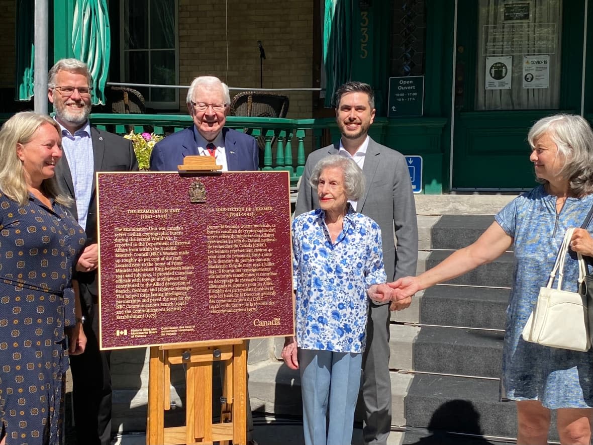 Sylvia Gellman, 101, stands next to a plaque commemorating the Examination Unit, the codebreaking bureau where she worked during the Second World War. Her hand is held by Julie McInnes, whose mother, Rita Bogue, also had a job there. (Joseph Tunney/CBC - image credit)