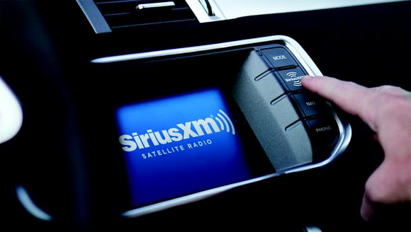 A driver touching the car interface of a Sirius XM radio display.