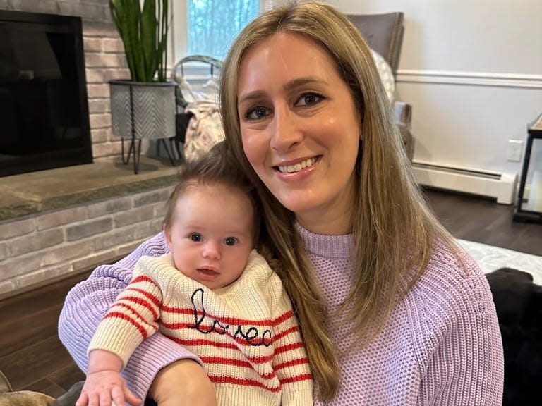 A mom holding her baby with a.fireplace behind them.