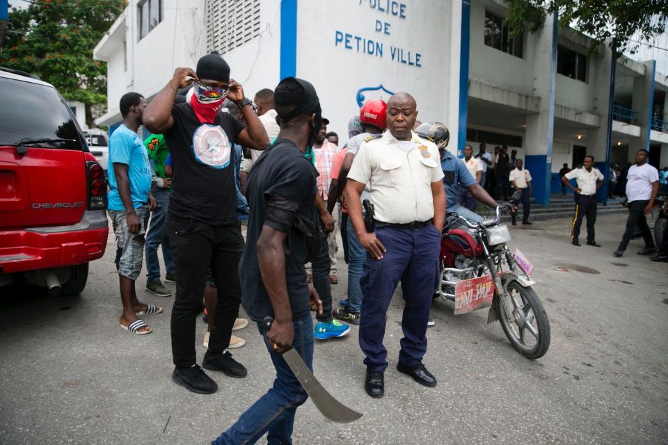 An angry protester holds up a machete as he asks for the fate of a policeman that was rumored to have been detained at the police station of Petion-Ville, as armed off-duty police officers protest over pay and working conditions, in Haiti, Monday, Feb. 24, 2020.