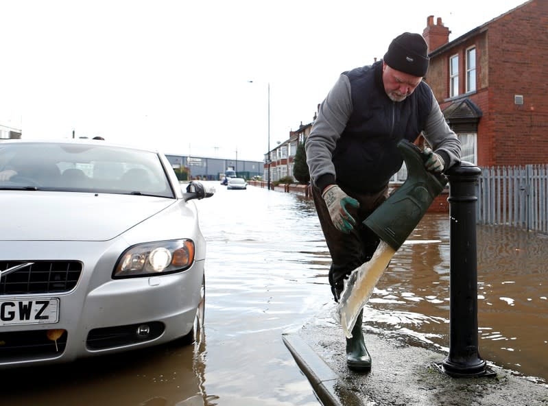 A man pours water out of his rubber boot on a flooded street in Bentley