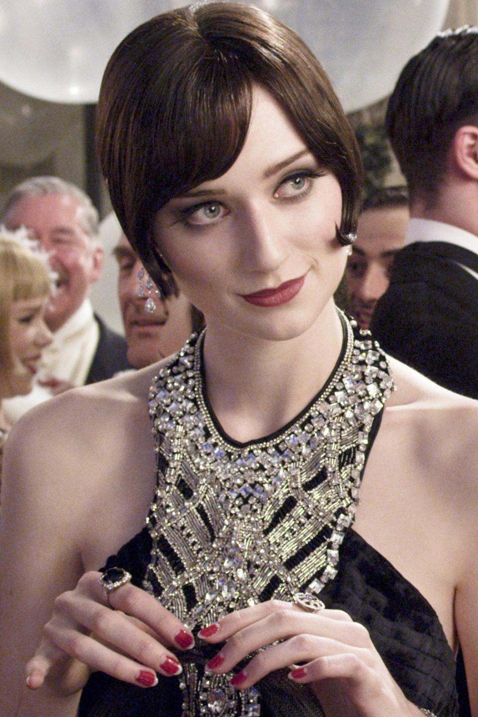 A glamorous woman in a lavish beaded gown stands amid an elegant party scene, engaged in conversation with other guests dressed in formal attire