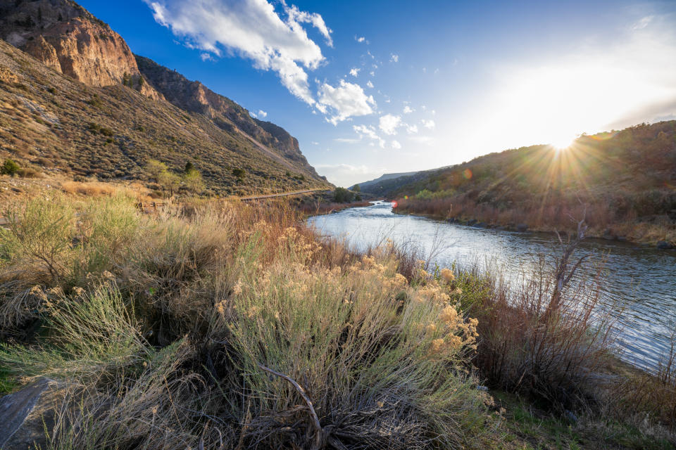 Sunset over a river with rocky cliffs on either side and grassy foreground