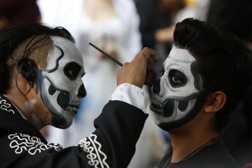 Ulises Armendariz, left, paints a customers face like a skull before the Catrinas parade down Mexico City's iconic Reforma avenue during Day of the Dead celebrations, Saturday, Oct. 26, 2019. (AP Photo/Ginnette Riquelme)