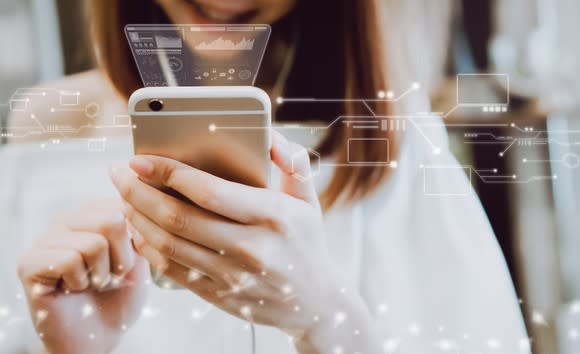 Woman using a smartphone with technological displays in the background.