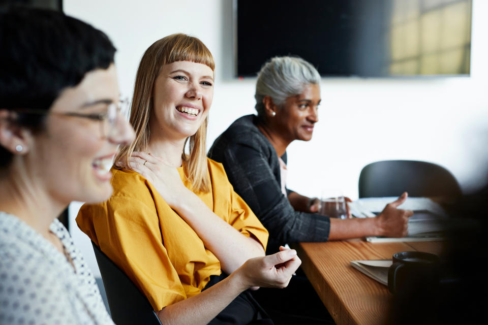 three women of varying agessit at a meeting together, smiling