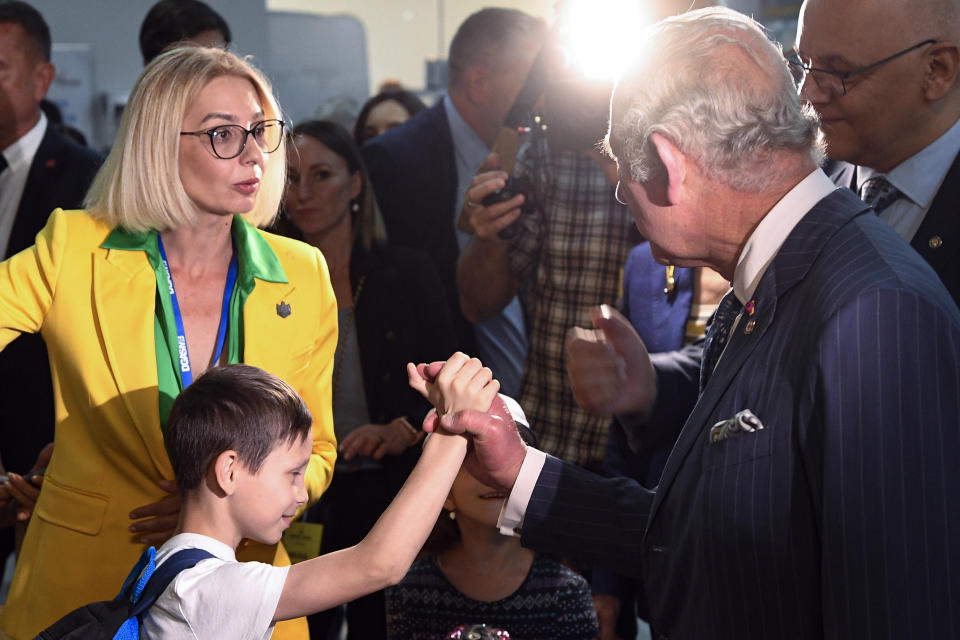 Britain's Prince Charles holds the hand of a child during a visit at a center for refugees fleeing the war in neighboring Ukraine, at the Romexpo convention center, in Bucharest, Romania, Wednesday, May 25, 2022. (Alex Micsik/Pool via AP)