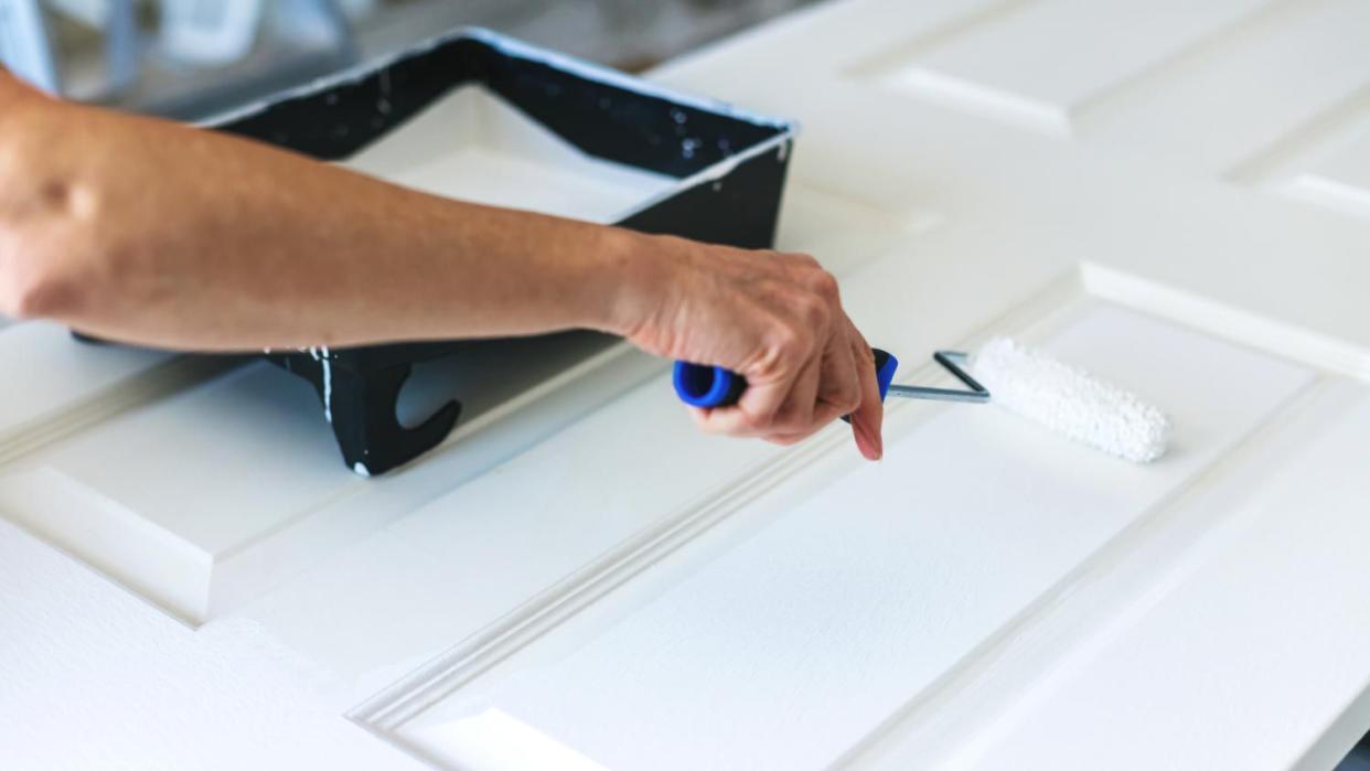 A woman painting a door with a roller