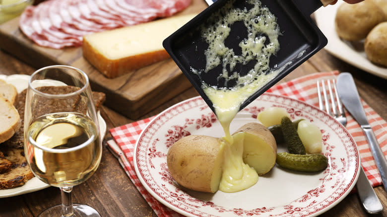 raclette poured over potatoes with wine and cornichons