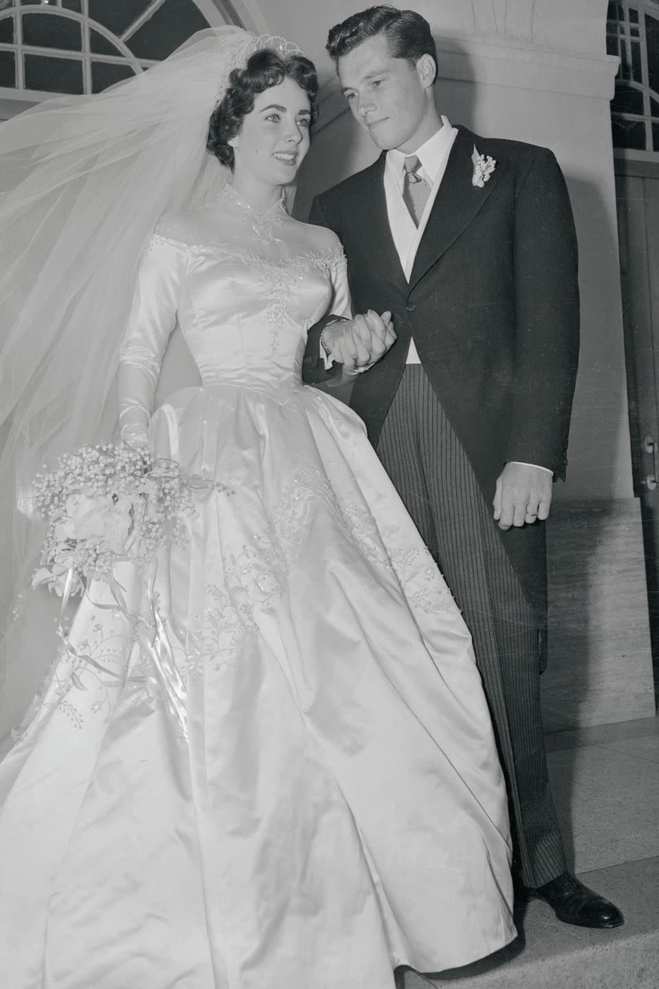 <p>Liz was married eight times to seven husbands — but her first time down the aisle was with Conrad “Nicky” Hilton when she was 18. She wore a satin long-sleeved gown with a silk gauze off-the-shoulder illusion neckline that was designed by MGM costume designer Helen Rose.</p><p><strong>RELATED</strong>: <a href="https://www.goodhousekeeping.com/life/entertainment/g2632/rare-photos-elizabeth-taylor/" rel="nofollow noopener" target="_blank" data-ylk="slk:60 Rare Photos of Elizabeth Taylor Through the Years;elm:context_link;itc:0;sec:content-canvas" class="link ">60 Rare Photos of Elizabeth Taylor Through the Years</a></p>