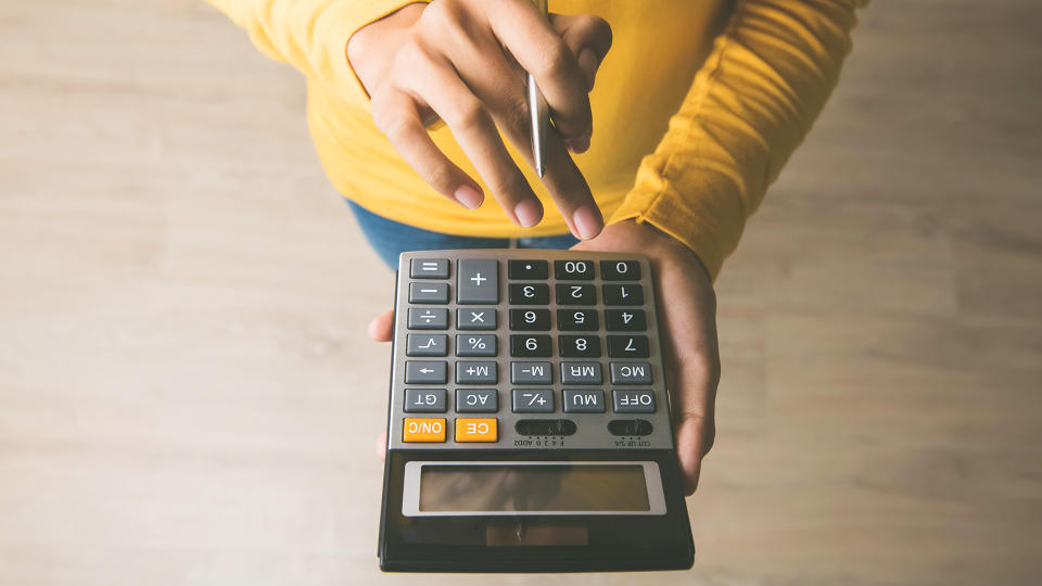 Woman entrepreneur using a calculator with a pen in her hand, calculating financial expense at home office - Image.