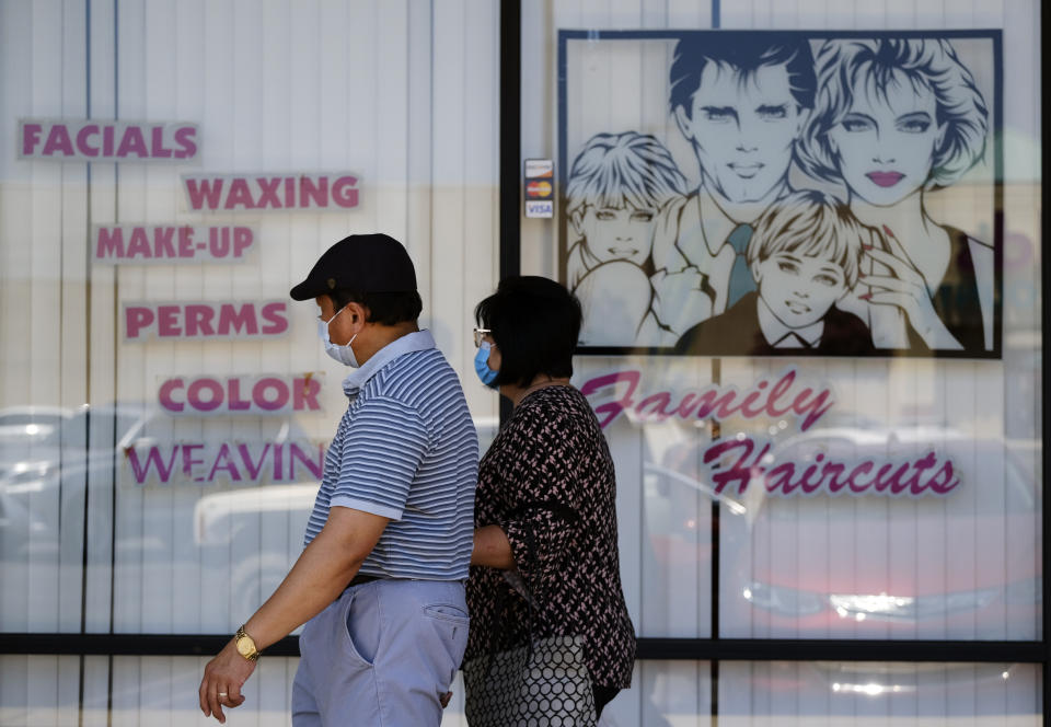 A couple wearing protective masks from coronavirus walk by a closed hair salon in the Panorama City section of Los Angeles on Tuesday, July 14, 2020. As the coronavirus swept California with renewed ferocity, the governor once again closed bars, inside dining and, for much of the state, gyms, indoor church services and hair and nail salons in an effort to prevent COVID-19 cases from swamping hospitals. (AP Photo/Richard Vogel)