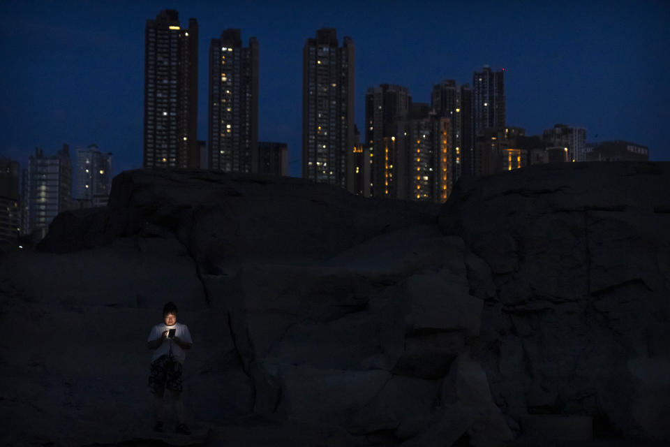 FILE - A woman uses her smartphone as she stands on a rocky outcropping normally submerged in the channel of the Yangtze River in southwestern China's Chongqing Municipality, Friday, Aug. 19, 2022. The very landscape of Chongqing, a megacity that also takes in surrounding farmland and steep and picturesque mountains, has been transformed by an unusually long and intense heat wave and an accompanying drought. (AP Photo/Mark Schiefelbein, File)