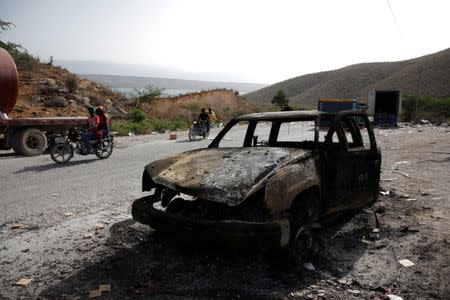 People riding motorbikes pass by a burnt car outside of the customs facilities in Malpasse, Haiti, July 8, 2018. REUTERS/Andres Martinez Casares