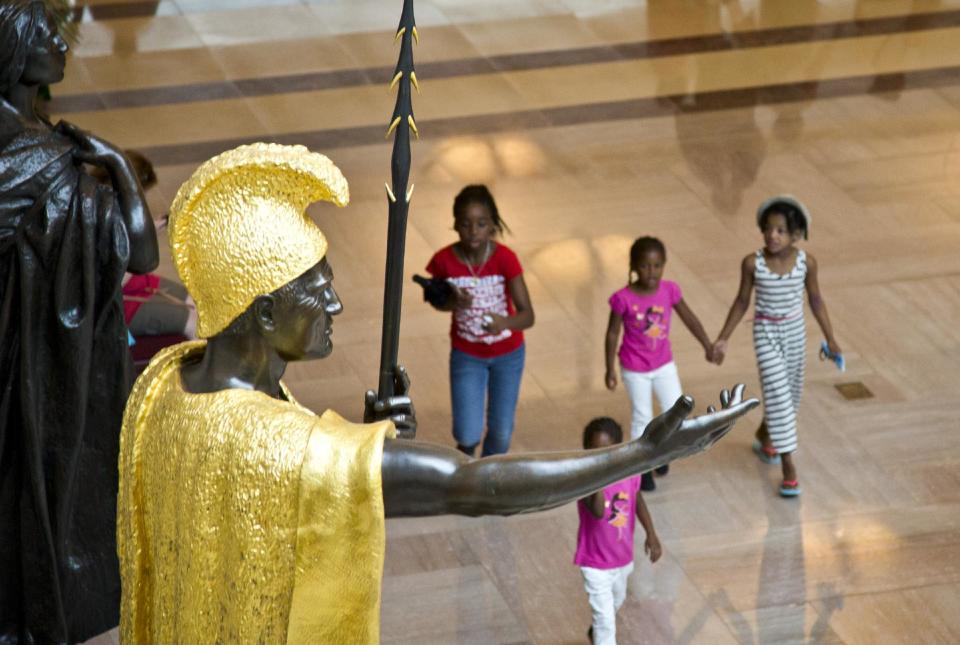 Young tourists walk beneath the towering bronze statue of King Kamehameha, the 18th century Hawaiian warrior-monarch, at the Capitol Visitors Center in Washington, Tuesday, July 2, 2013. American sculptor Thomas R. Gould depicted Kamehameha in his gilded robe and loincloth. It is the heaviest statue in the National Statuary Hall Collection. (AP Photo/J. Scott Applewhite)