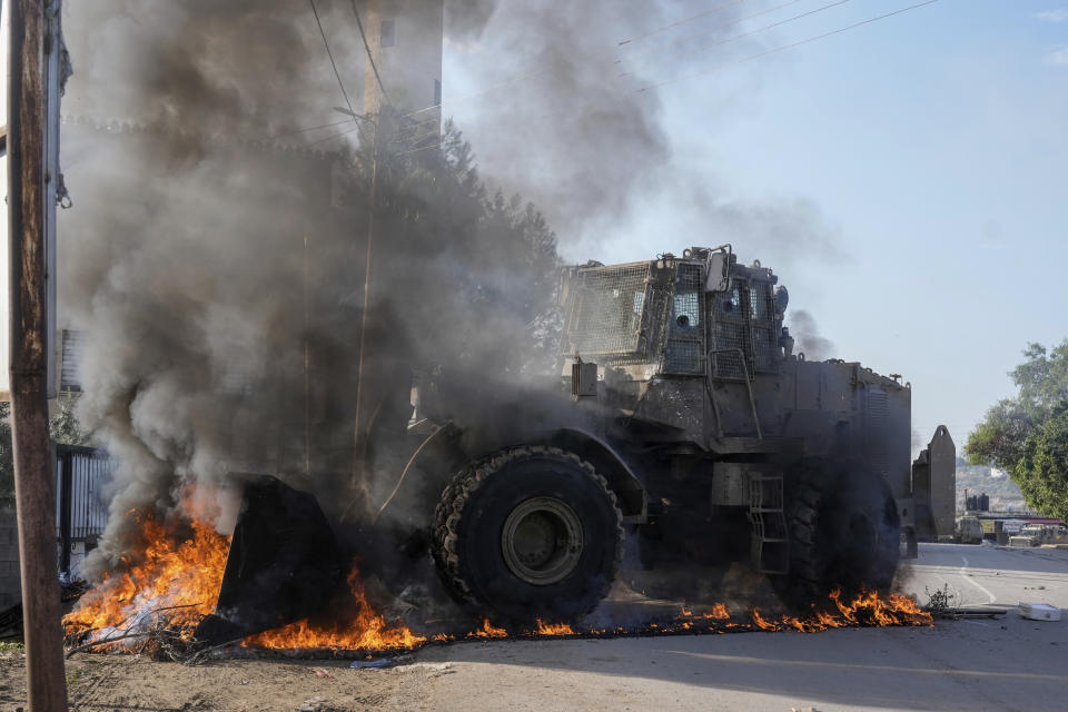 An Israeli army vehicle removes tires blocking roads that Palestinians had set on fire during a military raid into Faraa refugee camp, West Bank, Friday, Dec. 8, 2023. The Palestinian Health Ministry says that five Palestinians were killed when Israeli forces raided the camp prompting fighting with local militants. (AP Photo/Majdi Mohammed)