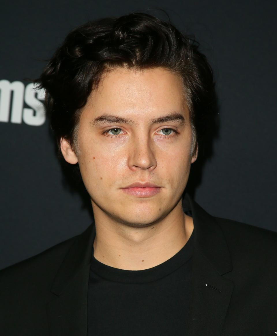 Sprouse poses for a photo while wearing a black T-shirt and black jacket