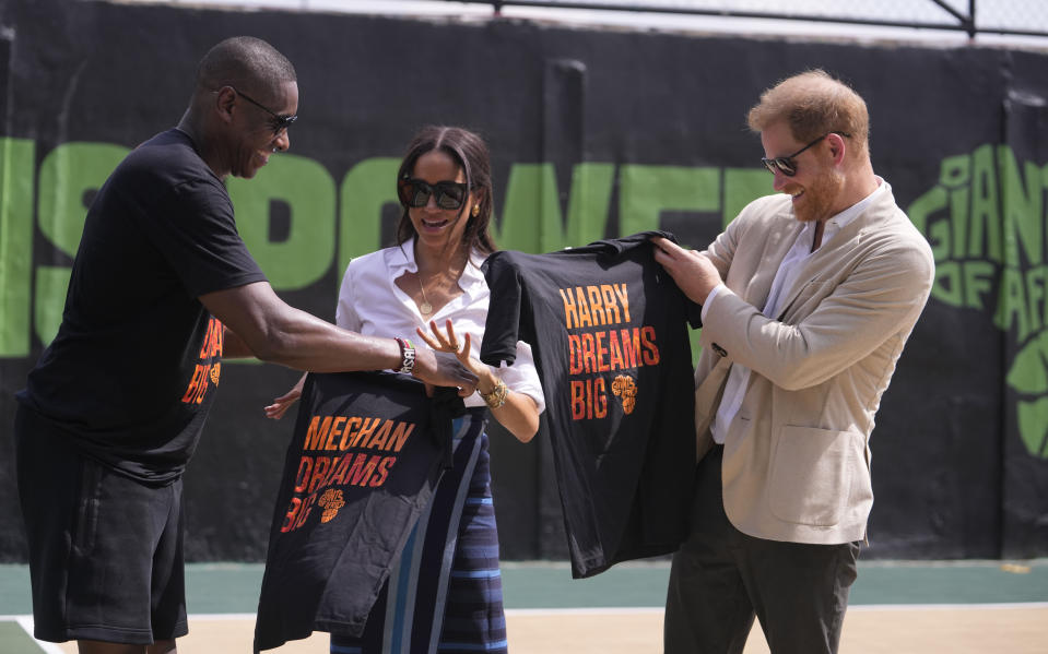 Masai Ujiri, Toronto Raptors President, left, presents T-Shirts to Prince Harry, right, and Meghan, center, during the Giant of Africa Foundation at the Dream Big Basketball clinic in Lagos Nigeria, Sunday, May 12, 2024. Prince Harry and his wife Meghan are in Nigeria to champion the Invictus Games, which Prince Harry founded to aid the rehabilitation of wounded and sick servicemembers and veterans. (AP Photo/Sunday Alamba)