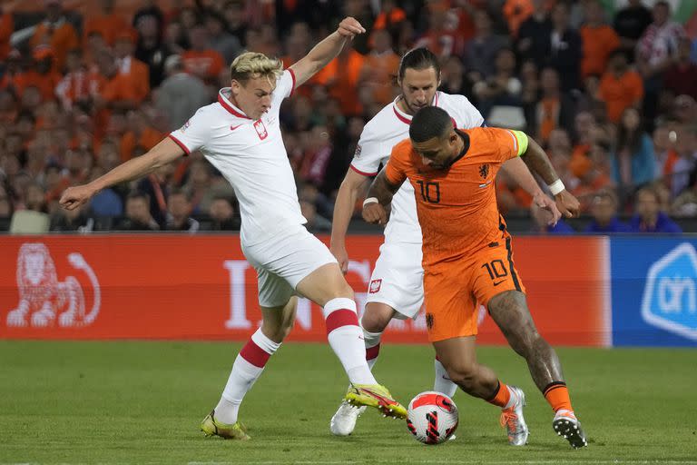 Memphis Depay, que desvió un penal en el final del partido, intenta dejar atrás a Szymon Zurkowski