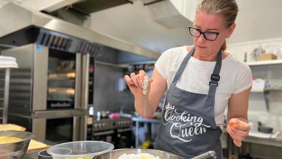 Romanian baker Nicoleta Radu prepares traditional Cozonac bread by pouring orange extract into a mixing bowl which has flour in it